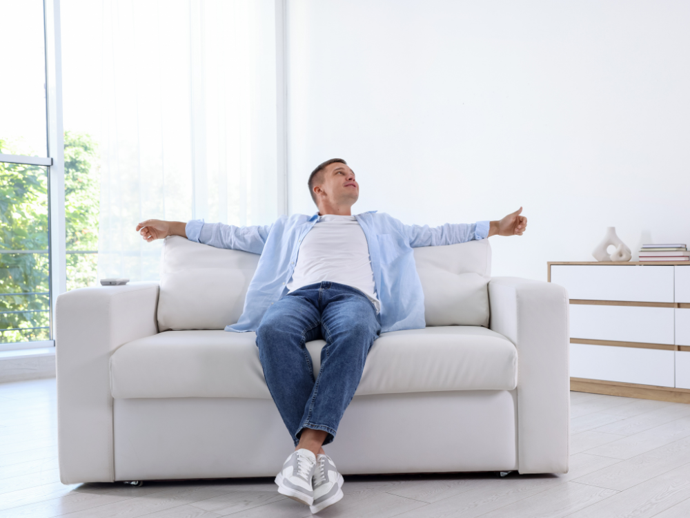 Jovem relaxando no sofá em sala moderna e iluminada, representando a busca por moradia e opções como **apartamento para alugar Blumenau** para quem ainda não consegue comprar casa própria.
