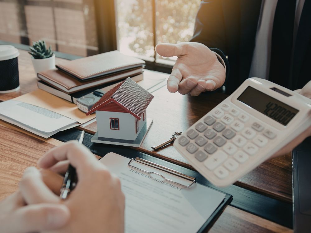 Pessoa analisando contrato e valores de financiamento imobiliário ao lado de maquete de casa e calculadora, representando a decisão sobre vale a pena comprar um apartamento financiado e planejamento para comprar apartamento Ribeirão Preto.